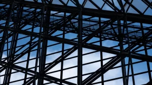 Estrutura metálica de treliças e vigas formando o esqueleto de um edifício, com o céu azul visível ao fundo.